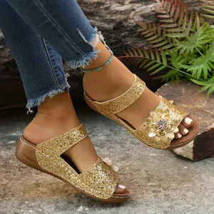 Close-up of golden glittery wedge sandals for women with floral detail and brown sole