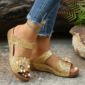Close-up detail of gold glitter wedge sandals with flower accent on model's feet.