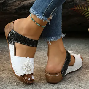 Close-up detail of wedge heel sandals with white flower and black croc-textured strap