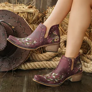 Detail view of floral embroidery and gold studs on burgundy Western ankle boots.