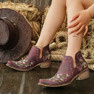 Detail view of ethnic floral embroidery and rivets on burgundy western ankle boots