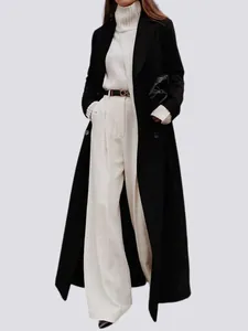 Detail view of a long black wool overcoat styled with white trousers