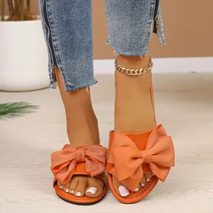 Vista detallada de las elegantes sandalias planas naranjas con un lazo decorativo