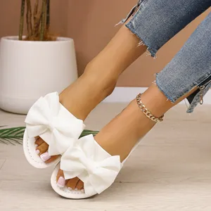 Primer plano de sandalias blancas con lazo combinadas con vaqueros y pulsera tobillera.
