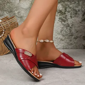 Close-up of elegant red faux leather wedge slippers for women with a decorative gold buckle detail