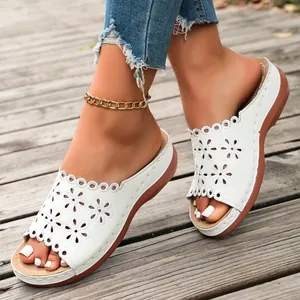 Close-up of white wedge sandals with laser-cut floral patterns and open-toe design