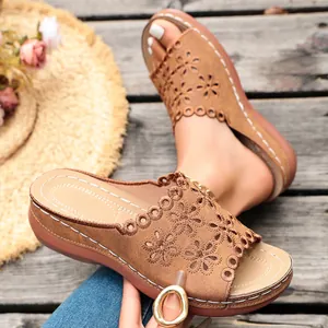 Detail of tan wedge sandals with intricate floral cutouts and white decorative stitching.