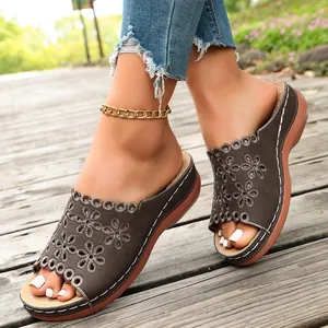Womens brown peep-toe wedge sandals with floral laser-cut detailing on outdoor wooden deck
