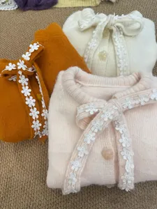 Dettaglio macro di cardigan in morbida maglia con elegante bordo in pizzo floreale bianco