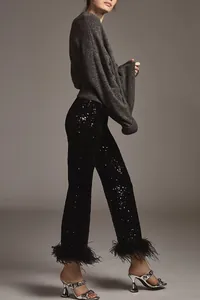 Full body view of black sequined trousers with ostrich feather hem and silver heels