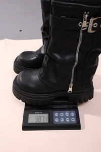 Close-up of black chunky leather boots on a scale showing 987.1g weight