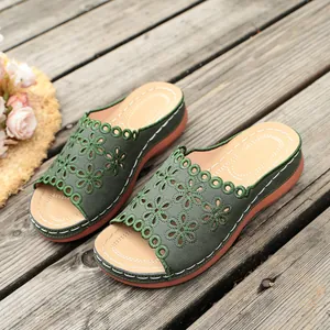 Detail view of stylish green platform slides with hollow-out floral embroidery patterns.