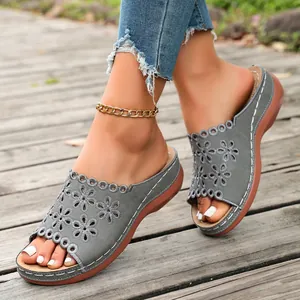 Detailed view of grey laser-cut floral wedge slides for women walking on a wooden deck