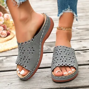 Detail of women's grey platform sandals with laser-cut floral patterns on a boardwalk.