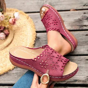 Close-up detail of burgundy wedge sandals with elegant floral laser-cut patterns on wooden deck.