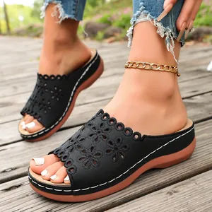 Detailed close-up of black floral laser-cut platform wedge slides on a wooden deck
