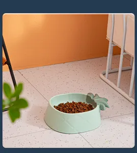 Close-up of a light green pineapple-shaped plastic pet bowl with cat food in a home setting