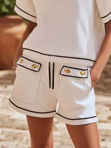 Close-up of white ribbed knit resort set with black piping and gold button details