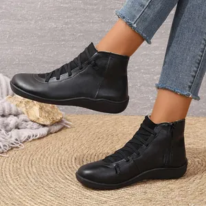 Vue latérale de bottines en cuir noir avec fermeture éclair et lacets sur un tapis de paille.