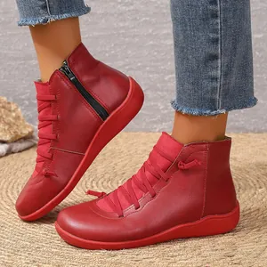 Détail montrant des bottines en cuir rouge avec fermeture éclair et lacets élastiques.