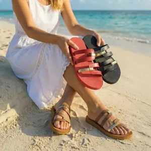 A woman wearing and holding colorful flat beach sandals on a sunny sandy shore in detail