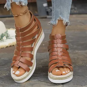 Detail of stylish brown gladiator sandals with platform rope sole on a stone surface.