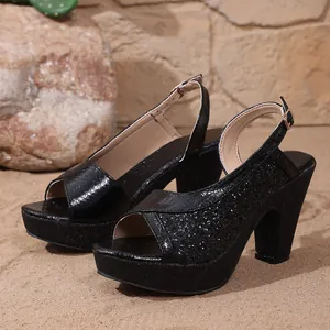 Close-up of black glittery platform high heel sandals on a natural sandy beach background.
