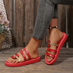 Red and gold flat sandals for women worn on feet against rustic wooden backdrop