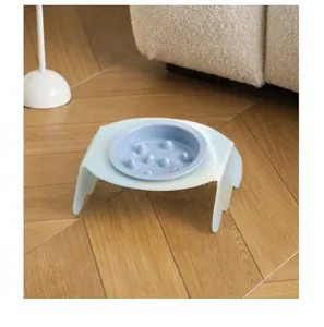 Detail view of blue ceramic slow feeder pet bowl with tilted acrylic stand on wood floor.