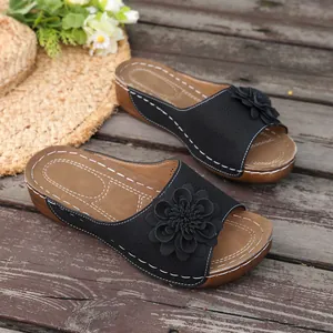 Detailed shot of black wedge slippers with 3D flower decoration on rustic wooden deck