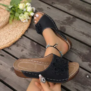Detail view of black wedge sandals featuring a 3D flower and contrast stitching