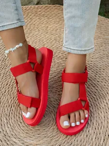 Gros plan de sandales à plateforme rouge vif avec brides velcro réglables sur les pieds.