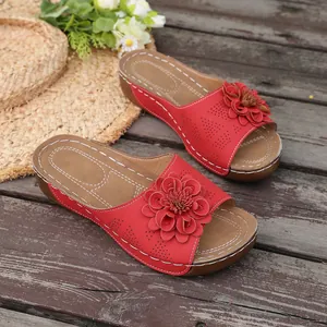 Close-up of red wedge sandals featuring a large decorative flower on a wooden deck