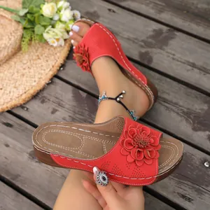 Close-up detail of red floral wedge sandals with white stitching on wooden background