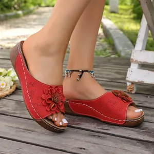 Close-up detail of red wedge slippers with decorative leather flowers and studs.