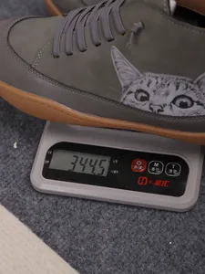 Detail van een grijze hoge schoen met kattenprint die op een weegschaal wordt gewogen.