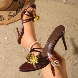 Eleganti sandali bordeaux con tacco a spillo e grande fiore in metallo dorato sulla spiaggia