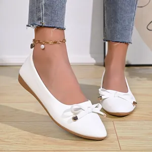 Elegant white pointed-toe ballet flats with delicate bow details worn by a model