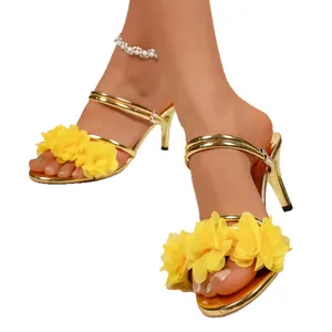 Elegant gold high-heeled sandals decorated with vibrant yellow fabric flowers on white background