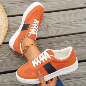 Détail de baskets décontractées orange pour femmes avec bande noire sur sol en bois