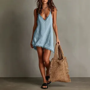 Model wearing a light blue V-neck mini dress with fringe trim and a straw tote bag
