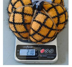 Detailed view of a knitted Halloween pumpkin weighing 210 grams on a digital kitchen scale.