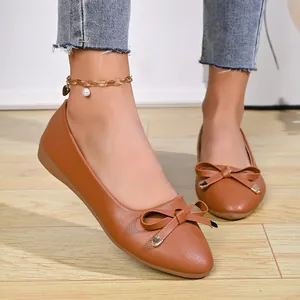 Detailed view of elegant brown pointed-toe flat shoes with decorative bow on a wooden floor