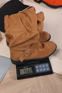Detail view of brown suede slouchy western boots with buckle being weighed on a scale