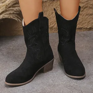 Detailed view of black suede Western ankle boots with embroidery worn on a stone floor
