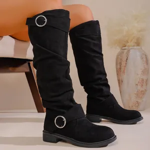 Close-up detail of black slouchy knee-high boots with decorative silver buckle straps