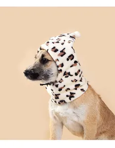 Leopard print plush dog hat with white pom-pom detail on beige background