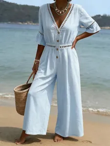 Macro detail of a light blue V-neck jumpsuit featuring white lace trim on a beach