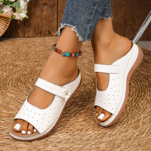Nahaufnahme weißer Keilsandalen mit Blumenakzenten und perforiertem Leder auf Strohmatte