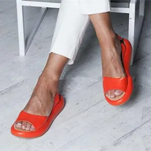 Primer plano de una modelo con sandalias planas naranjas con la punta abierta.